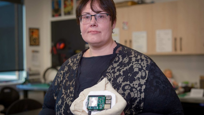 A woman stands holding a fabric prosthetic in her left hand.