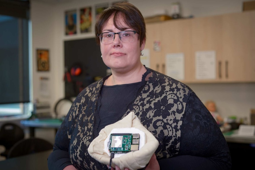 A woman stands holding a fabric prosthetic in her left hand.