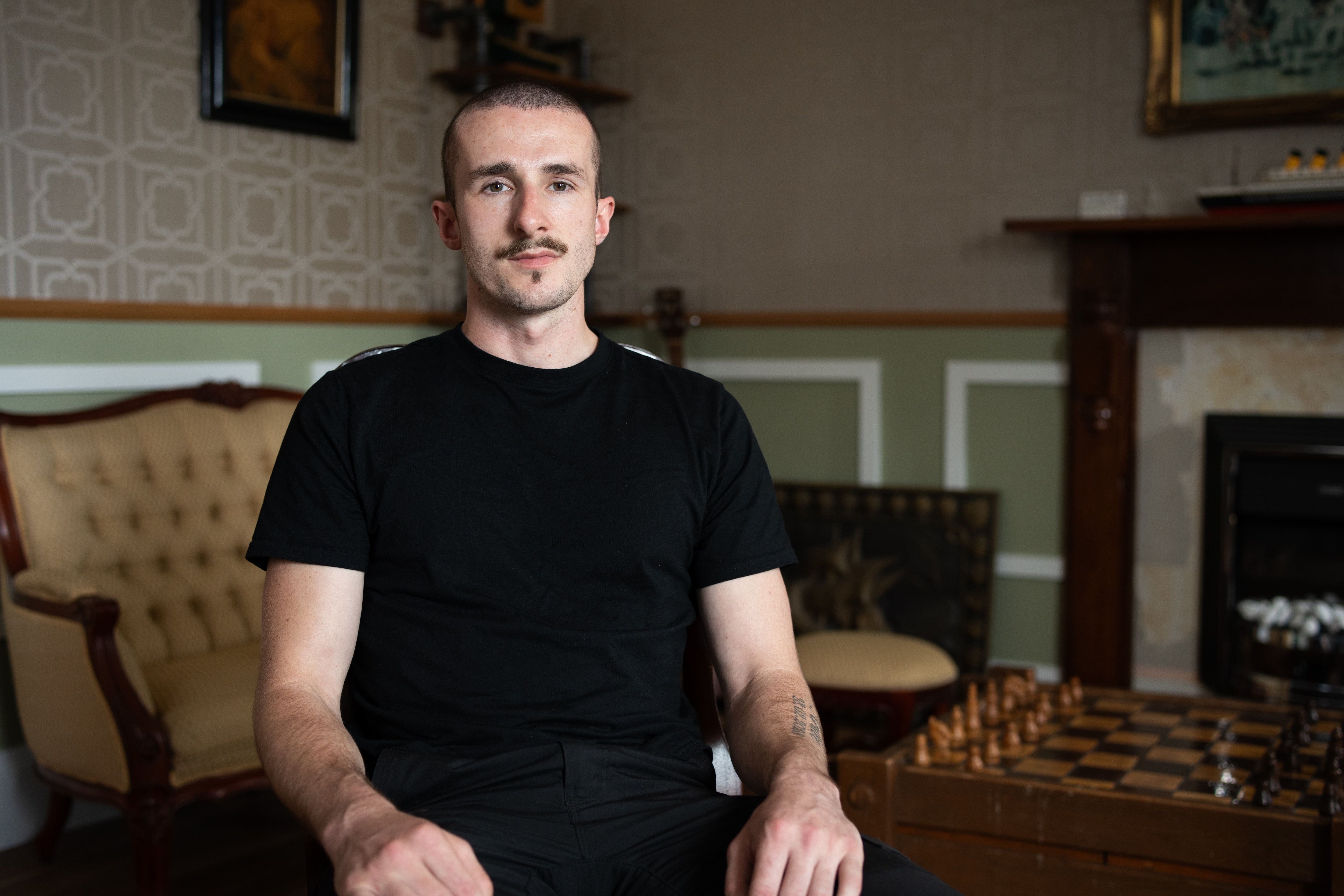 Um homem de camiseta e calça pretas senta-se para um retrato.