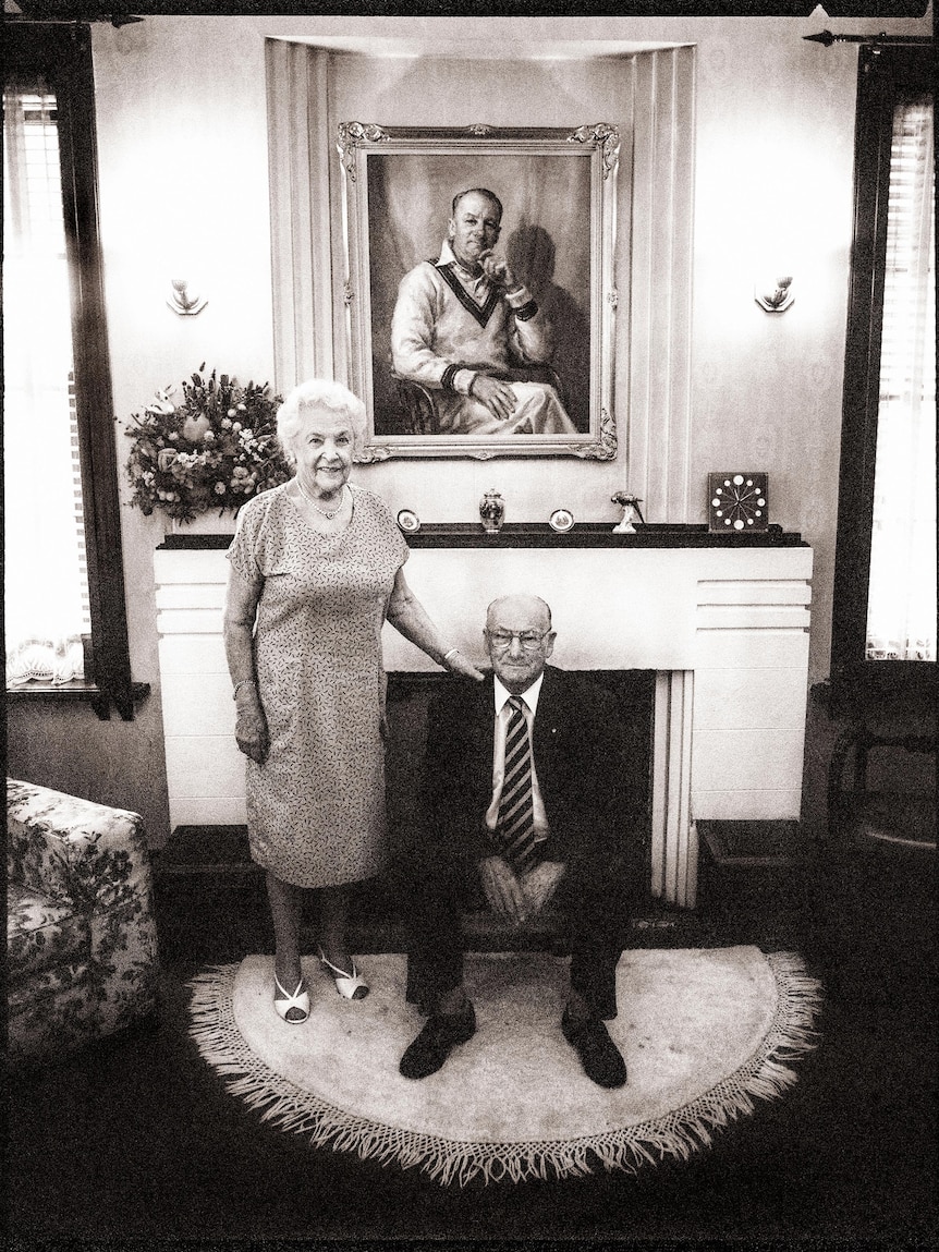 Sir Don sits in a chair, Jessie standing beside him, both smiling in the black and white image.