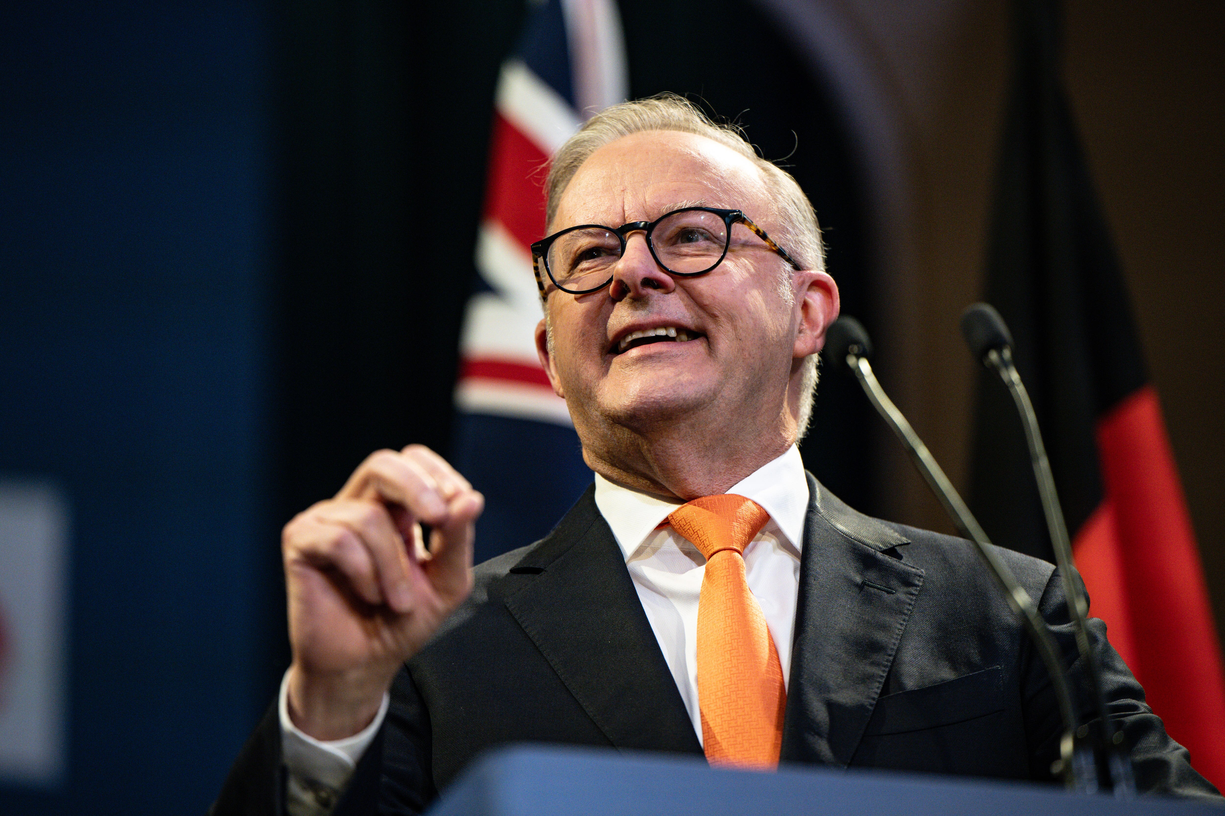 Albanese smiling at a lectern with Australian flag behind him