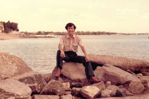 a man sitting on a rock near a bay.