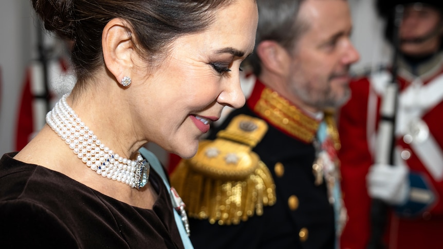 A close-up of the side of Princess Mary's smiling face, with Prince Frederik in the background