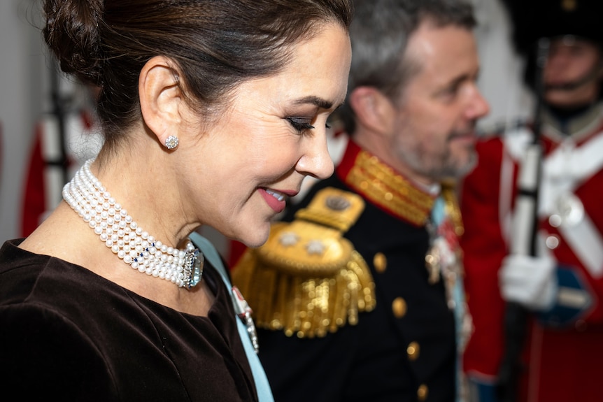 A close-up of the side of Princess Mary's smiling face, with Prince Frederik in the background