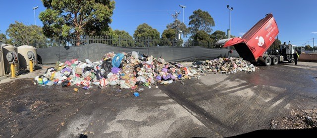 A large pile of rubbish that has been tipped out by a red rubbish truck.