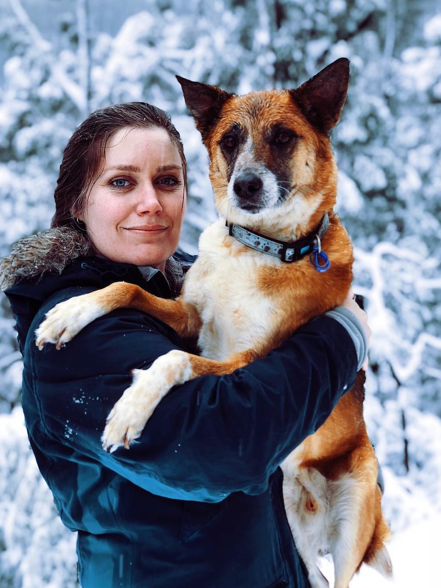 A woman holding up a dog and smiling.