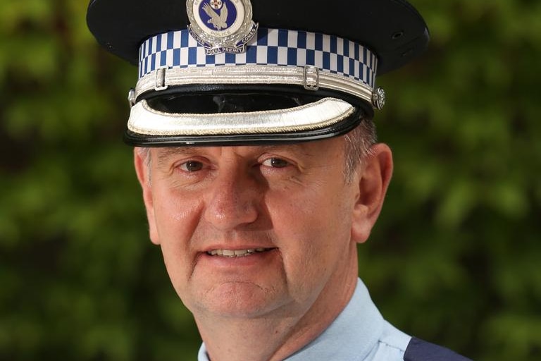 Headshot of police officer looking at camera. Green leafy background. 