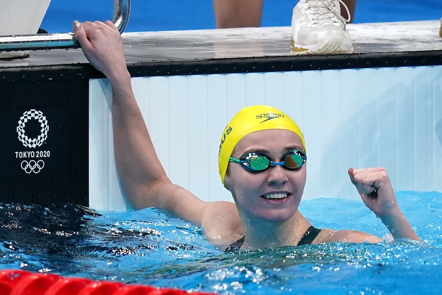 Ariarne Titmus, still wearing goggles in the pool, looks up and pumps her fist