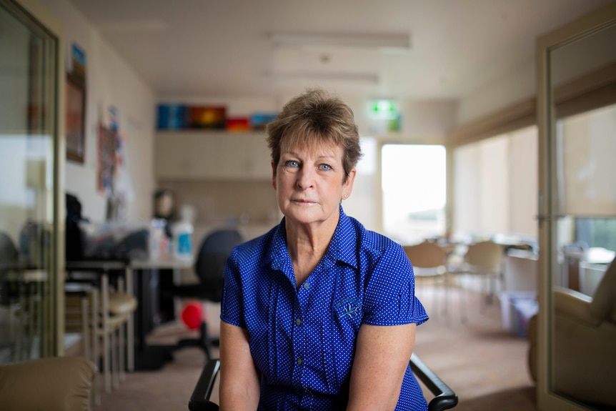 A middle-aged woman in a blue uniform sits on a chair