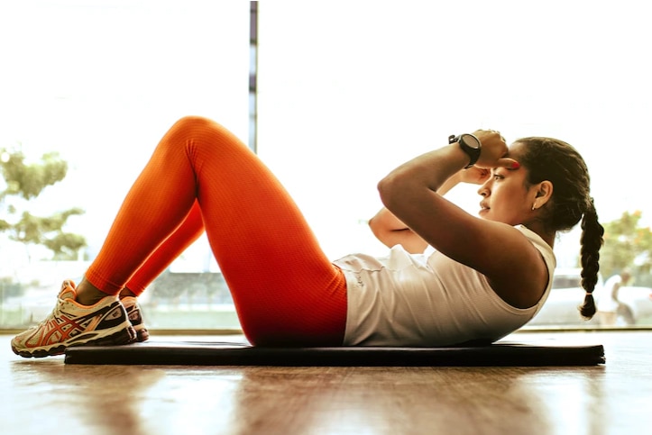 A woman lies on a yoga mat doing workout.