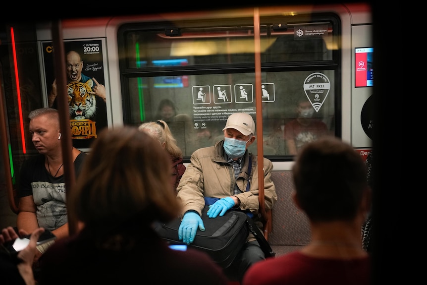 An older man wears a blue mask and gloves. A man next to him is not wearing a mask.