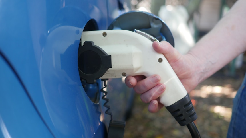A person holds a plug-in to charge an electric car. 
