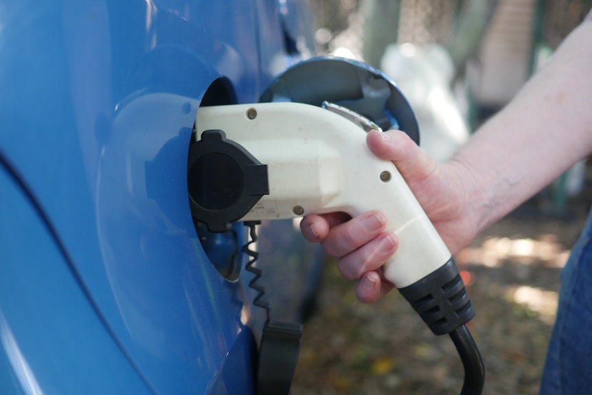 A person holds a plug-in to charge an electric car. 