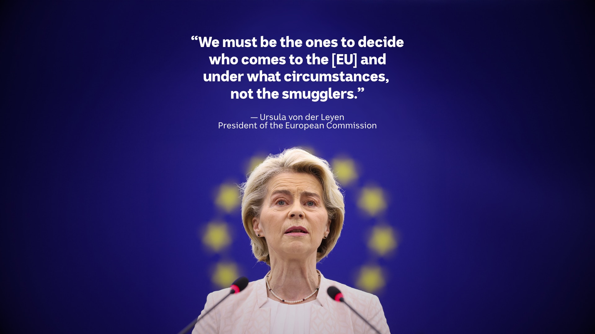 A blonde white woman in a pink blazer stands at a podium, with the EU flag behind her.