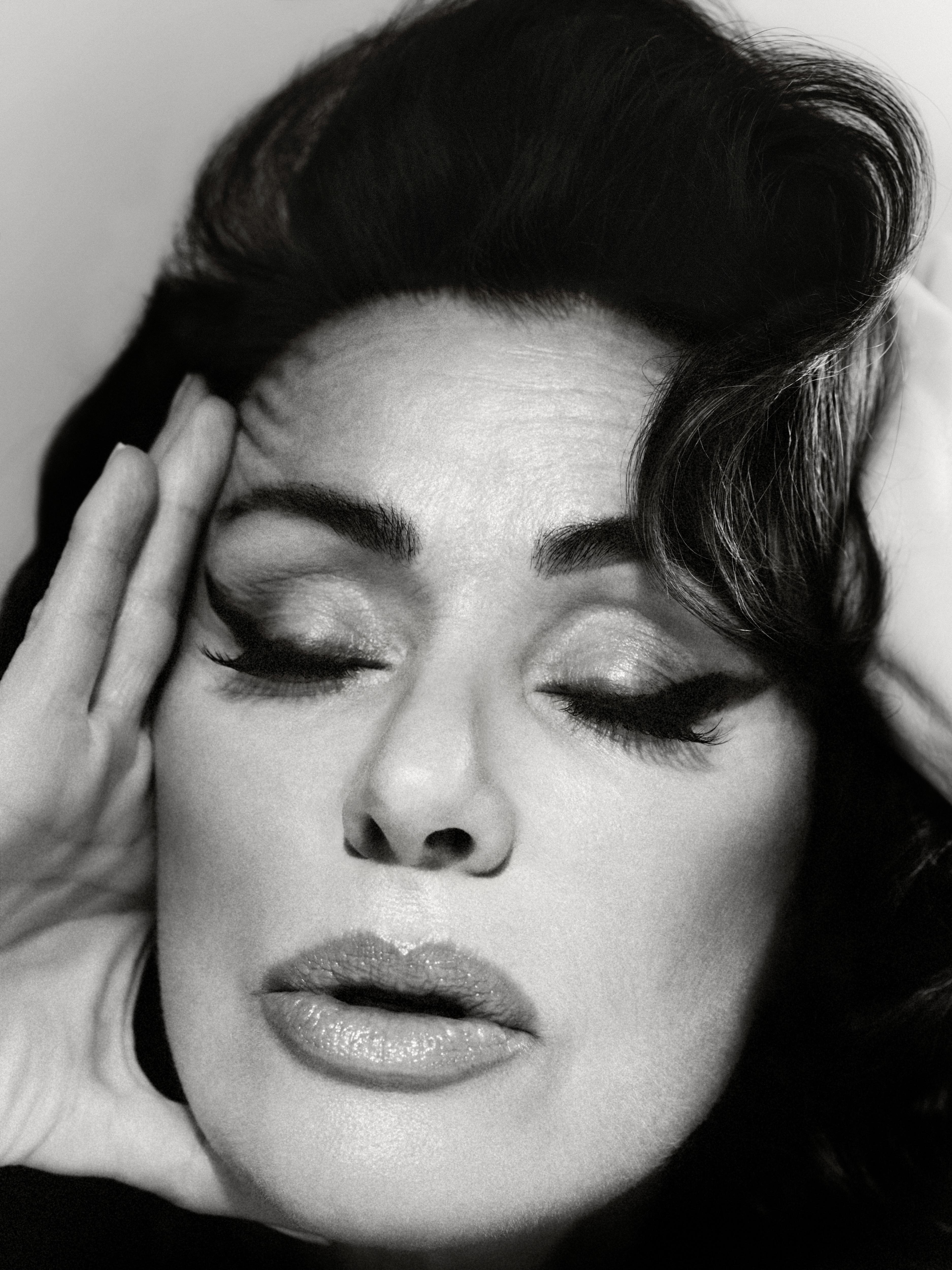 The black and white image is a close-up of Tina, wearing makeup, her eyes closed and her hand pressed to her palm.