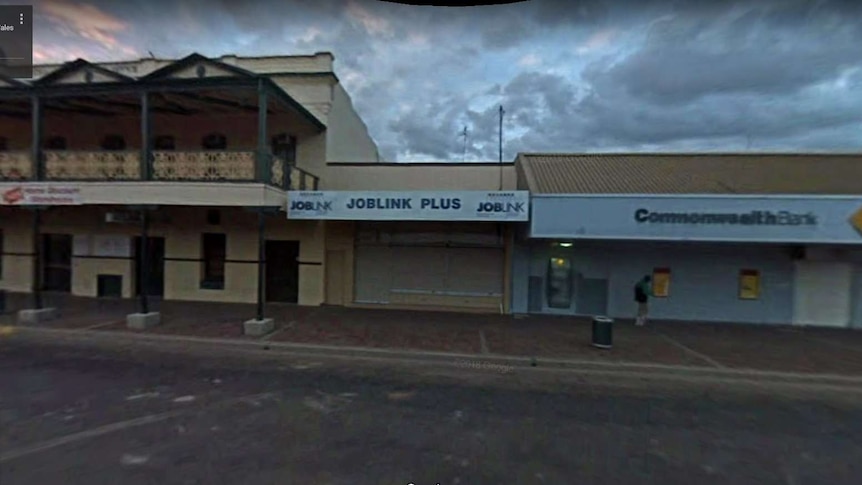 Blurry image of small office flanked by large bank building and corner two storey pub in main street of Bourke