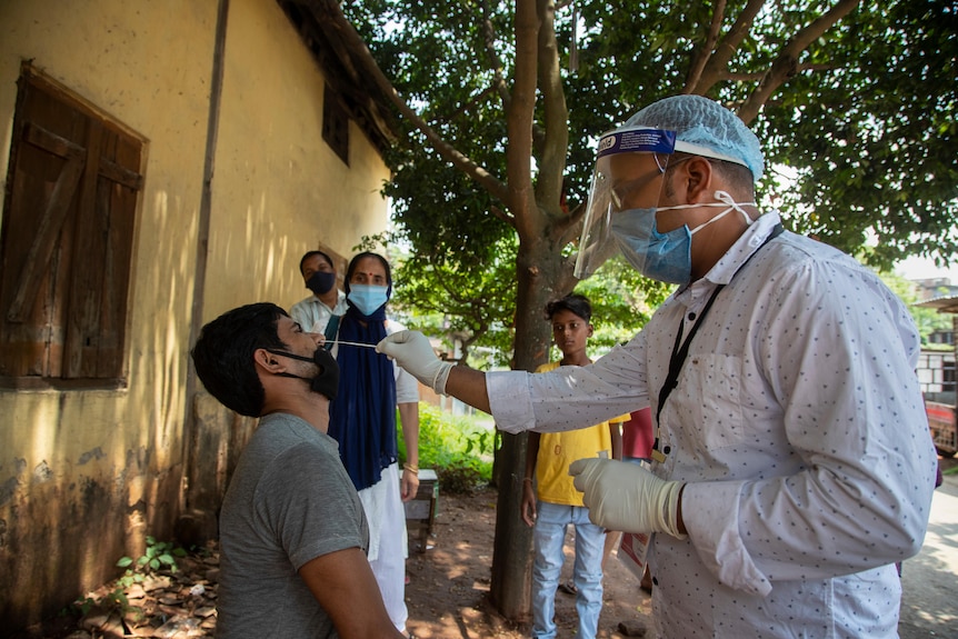 A person sits down and gets a nasal swab from a healthcare worker outside.