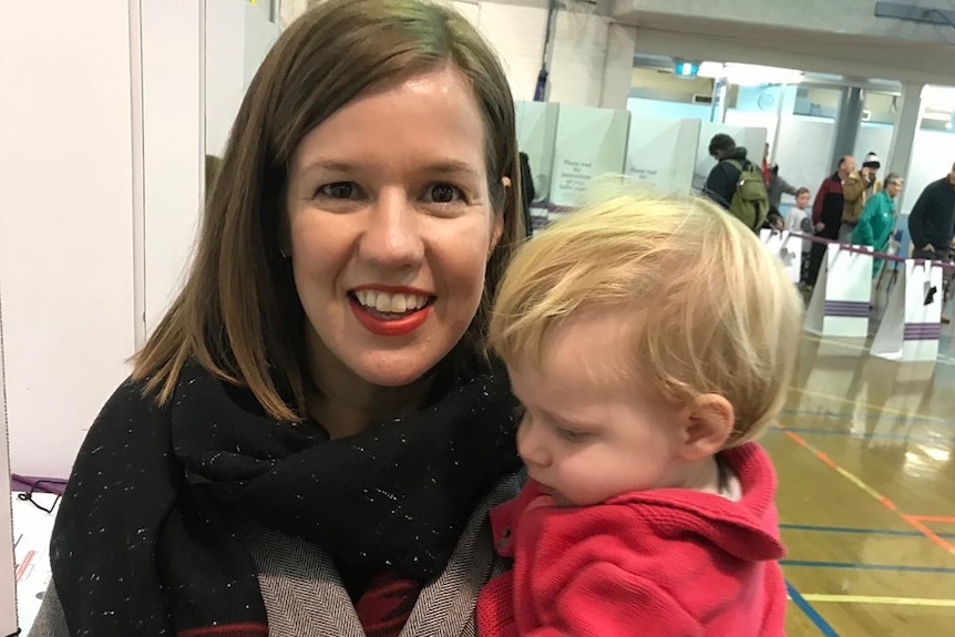 A woman poses for a photograph while holding a young child.