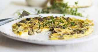Close up of an omelette or frittata with fresh herbs on a white plate and table setting.
