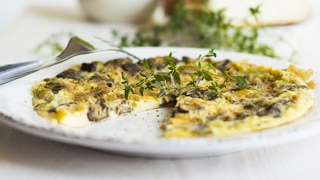 Close up of an omelette or frittata with fresh herbs on a white plate and table setting.