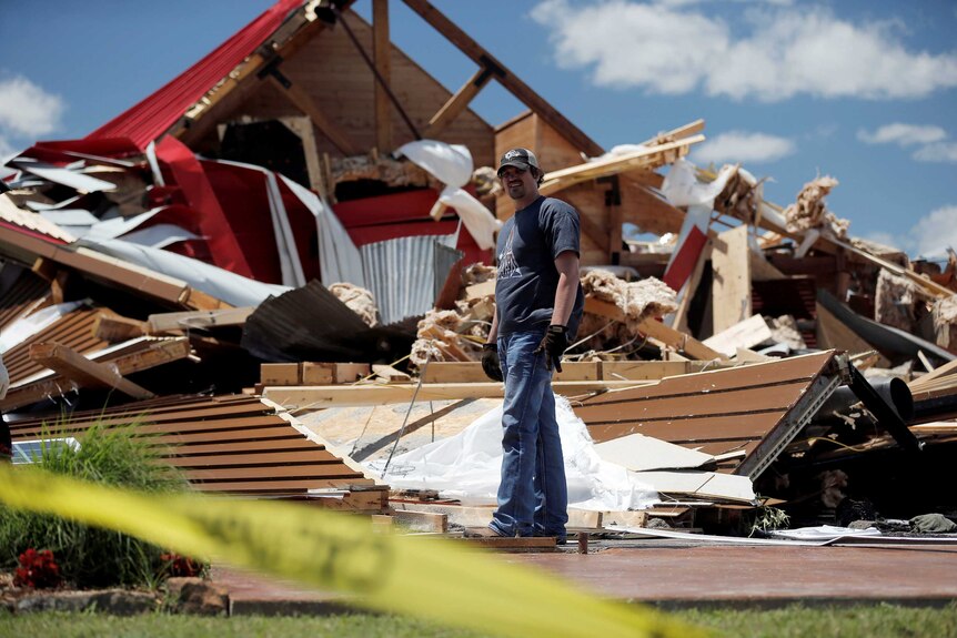 Man looks for belonging in the ruins of a barn destroyed by a tornado.
