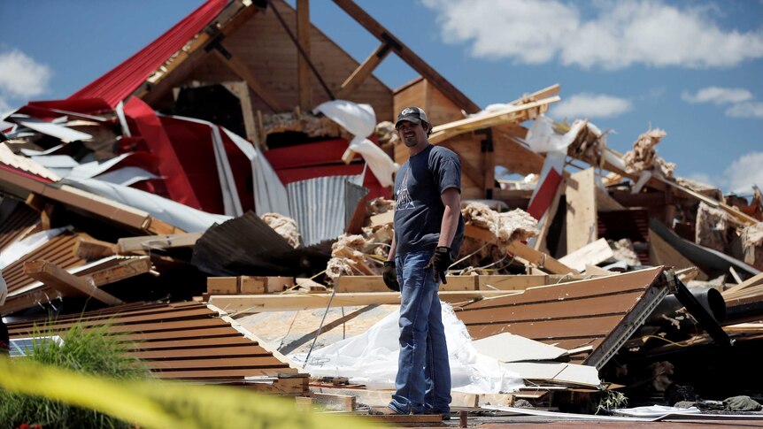 Man looks for belonging in the ruins of a barn destroyed by a tornado.