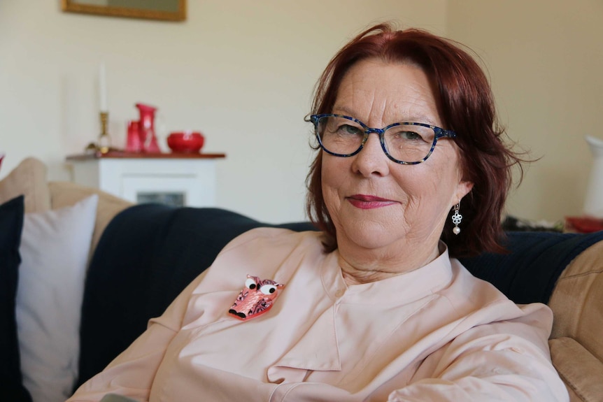 A woman, sitting in her home, smiles at the camera.