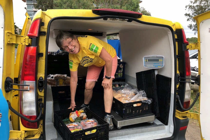Oz Harvest volunteer moves food crate from inside the back of a van.