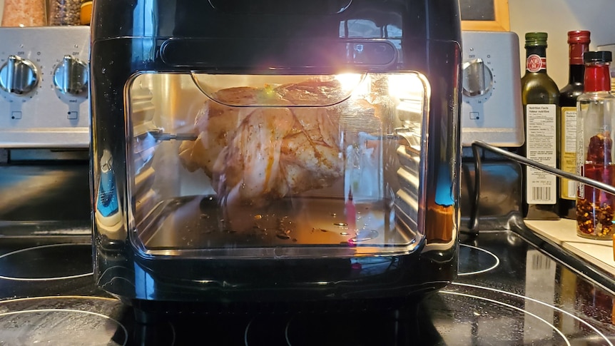 Air fryer oven sitting on top of large oven, roast chicken inside