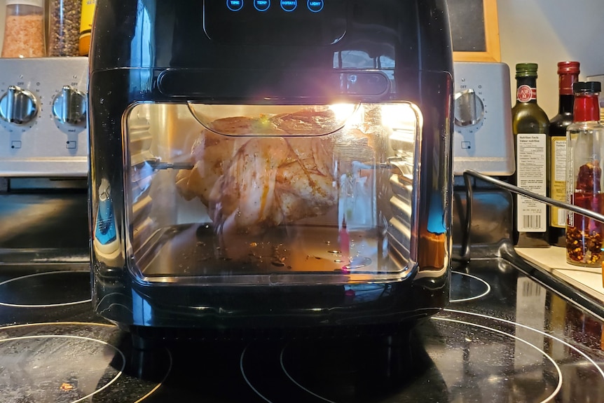 Air fryer oven sitting on top of large oven, roast chicken inside