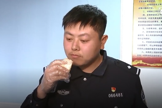 A Chinese police officer wears plastic gloves and eats a piece of durian.