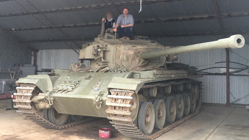 A man and boy sit atop a real military tank.