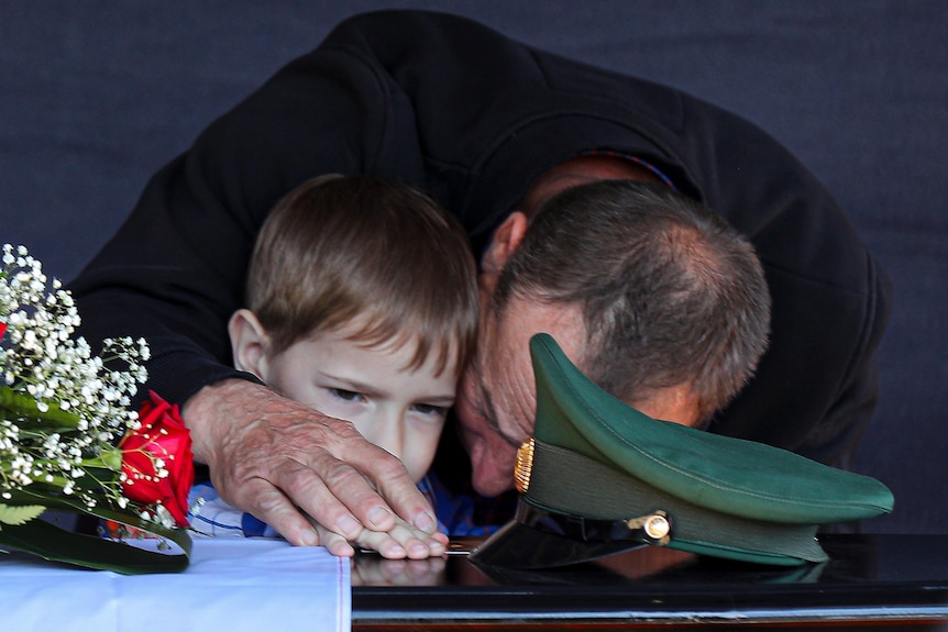 The father and son of a Russian soldier mourn his death. They are standing by his casket, crying.