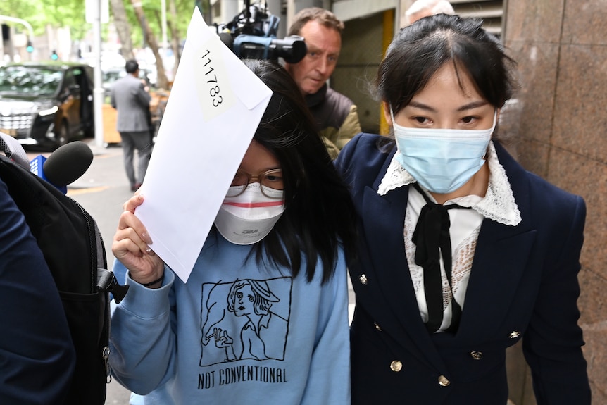 A woman holds an envelope over her face to obscure it as she leaves court