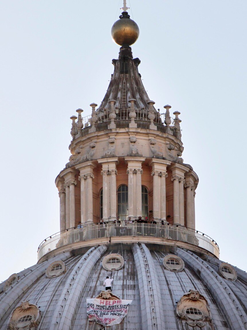 Marcello Di Finizio stands on the dome of Saint Peter's Basilica holding a banner.