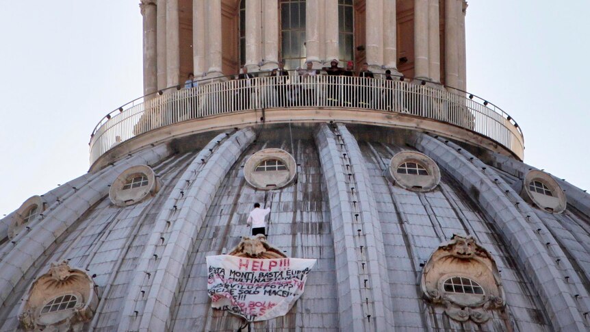 Marcello Di Finizio stands on the dome of Saint Peter's Basilica holding a banner.