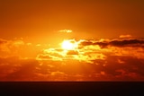 The sun in a cloudy sky sets over a beach