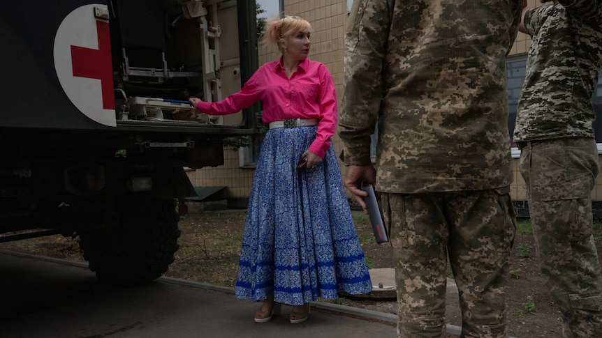 Left an army truck with a large red cross on the back, next to it an elegantly dress lady in heels and two soldiers on the right