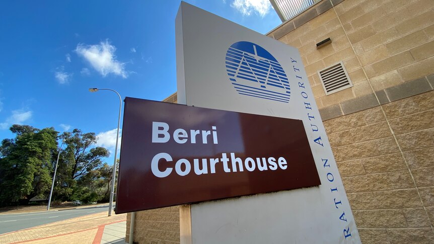 Outside of the Berri Magistrates Court, the sky is blue and the sign is dark brown.