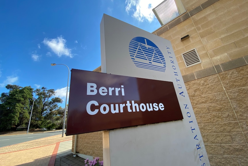 Outside of the Berri Magistrates Court, the sky is blue and the sign is dark brown.
