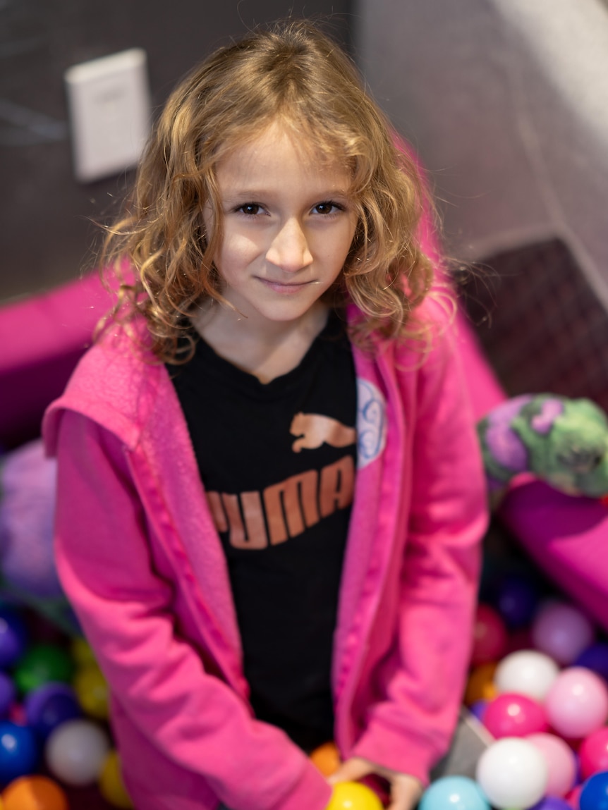 Young girl wearing black Puma shirt and pink hoodie in a ball pit.