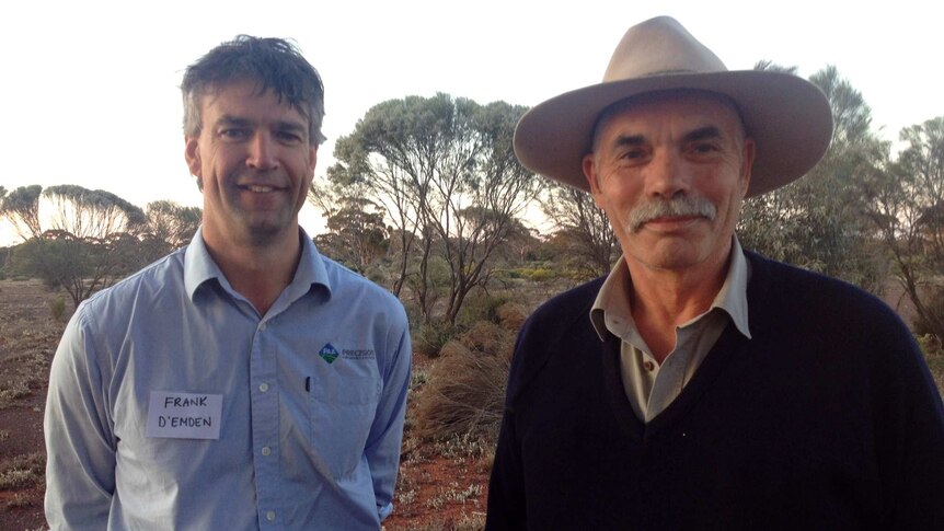Ross Wood stands in foreground with large akubra hat and Frank D'Emden stands in background among pastoral scrubland