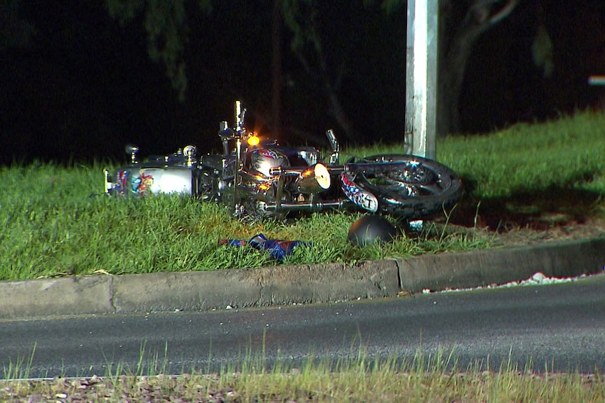 A damaged motorcycle on its side on the grass next to a lightpole