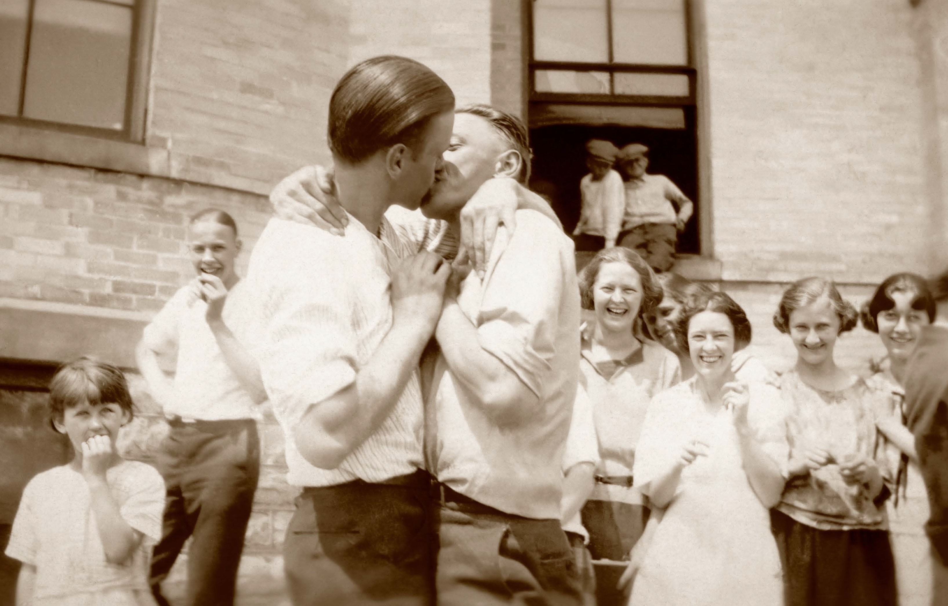 Una fotografía en blanco y negro de dos hombres besándose mientras la gente aplaude.