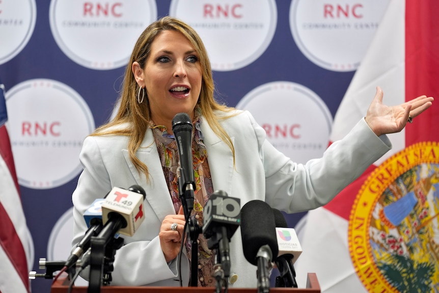 Ronna McDaniel gestures as she speaks at a table covered in microphones