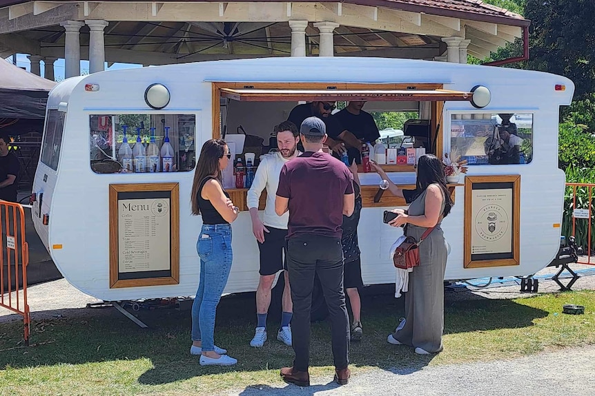 A group of customers standing in front of a coffee caravan waiting for their coffee.
