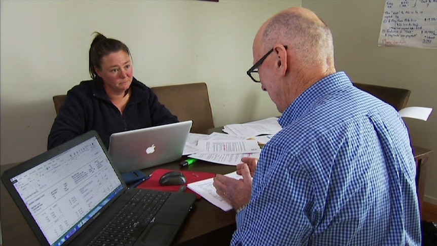 Dairy consultant John Mulvaney and farmer Bec Casey sit at a desk with computers and papers, drawing up a survival plan.