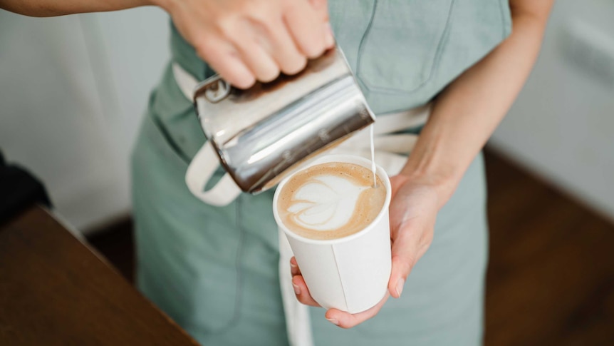 A barista pours milk into a takeaway coffee cup.