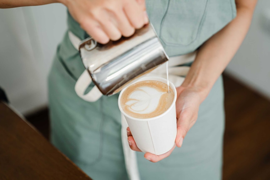 A barista pours milk into a takeaway coffee cup.