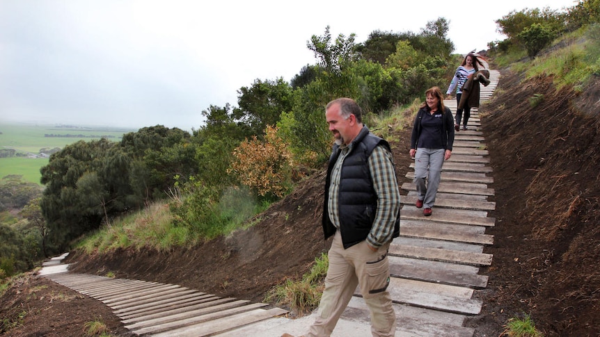 People walking down a steep walking trail on a hillside, the steps made out of limestone